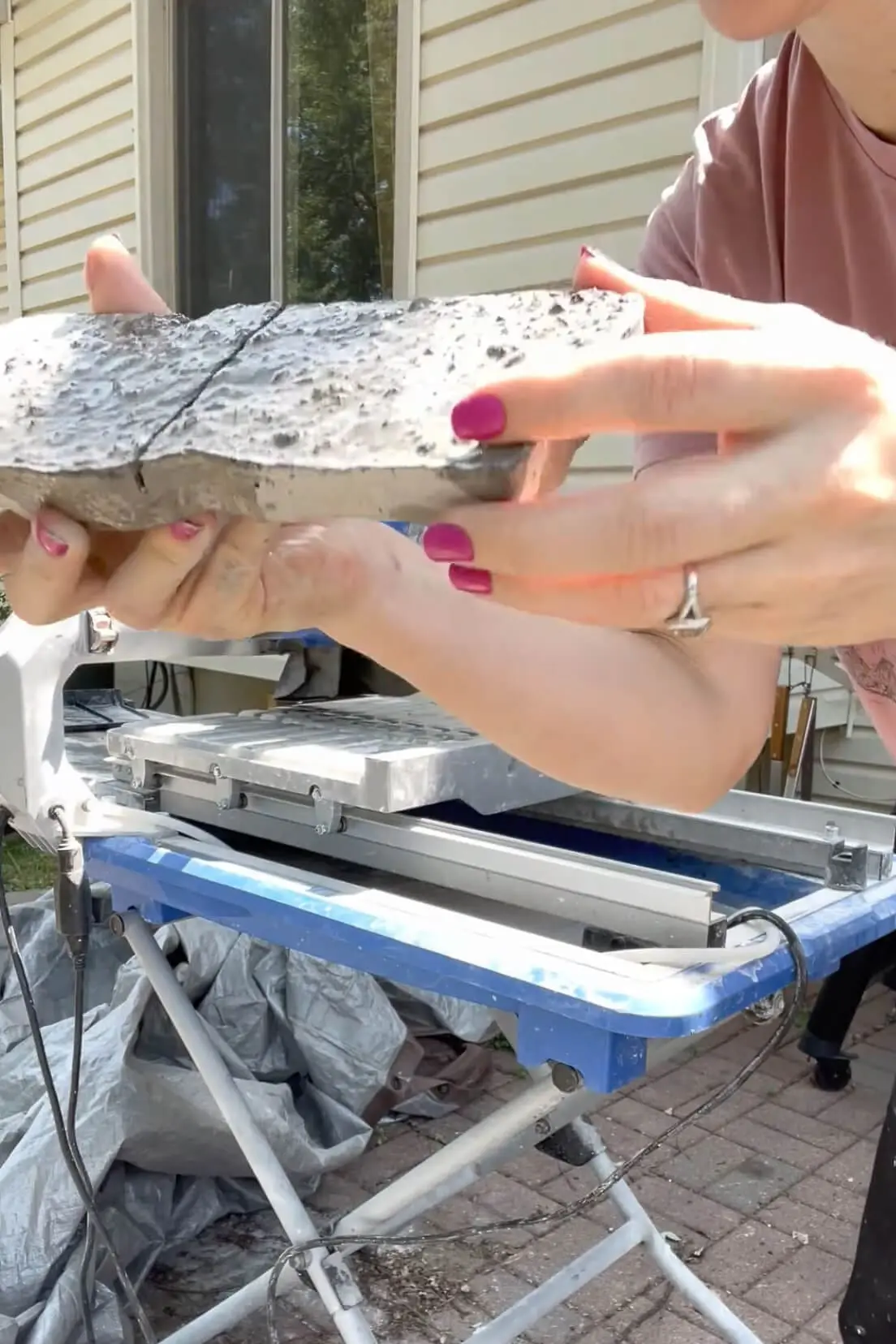 Hands holding a stone veneer piece with a visible crack after being cut on a wet saw.